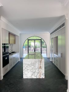 Modern kitchen renovation in Rose Bay with large natural marble island, custom cabinetry, dark timber parquet flooring, and arched glass doors.
