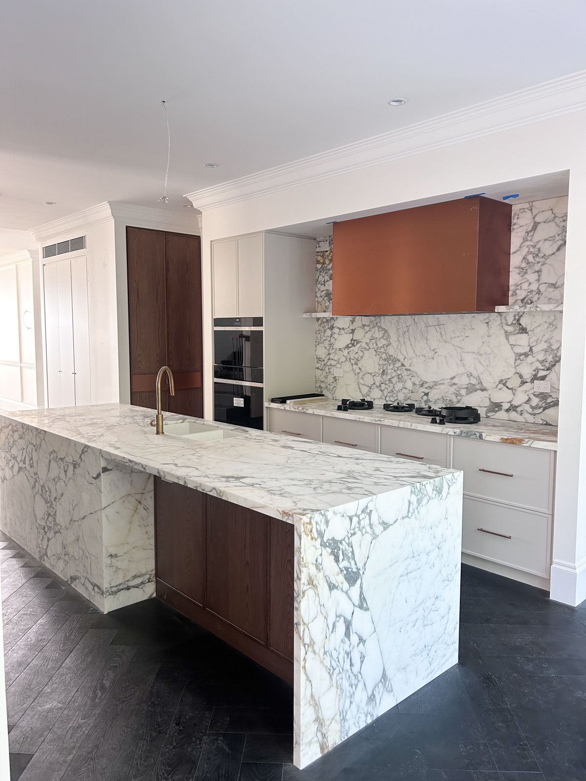 Modern kitchen renovation in Rose Bay with large natural marble island, custom cabinetry, dark timber parquet flooring, and arched glass doors.